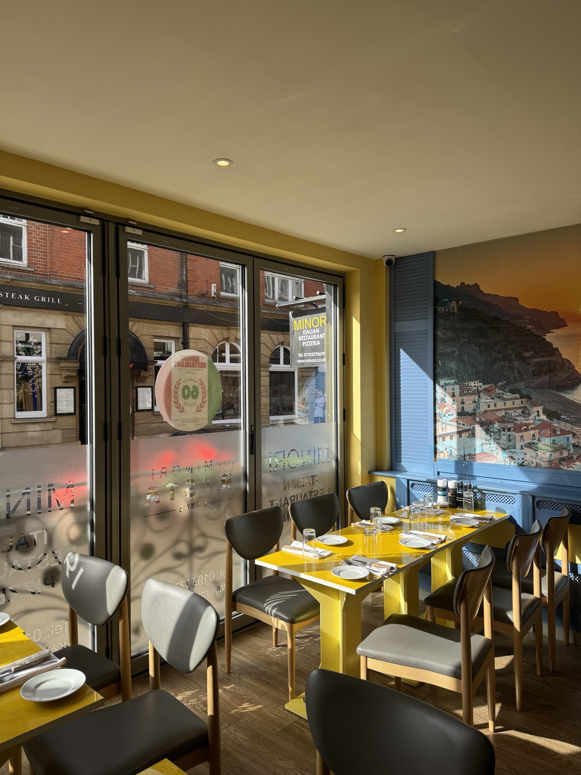Long yellow tables set for a party at Minori Rickmansworth, under the Amalfi Coast mural